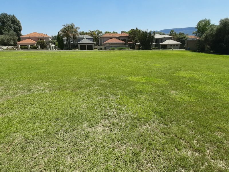 A wide, level residential vacant land plot featuring a well-maintained grass lawn with surrounding neighborhood homes in the background.