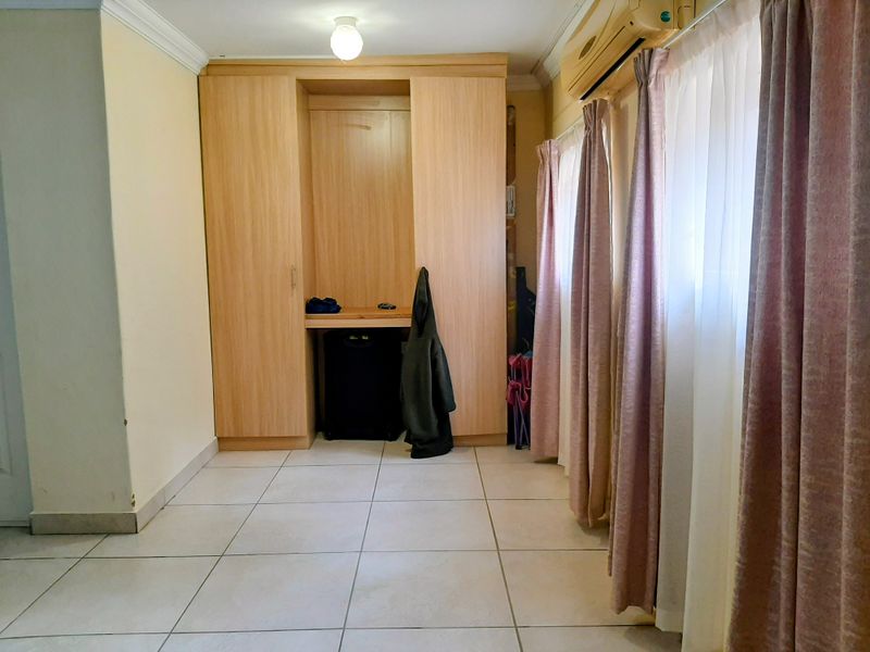 A bedroom featuring light-toned built-in cabinetry, tiled flooring, and a wall-mounted air conditioning unit.