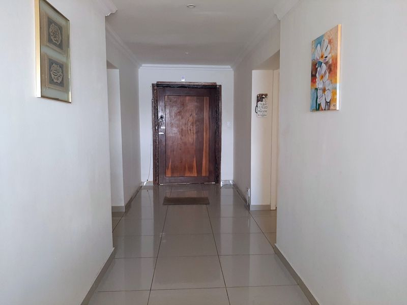 A bright and spacious entrance hallway featuring neutral tiled flooring, clean white walls, and a solid wood front door.