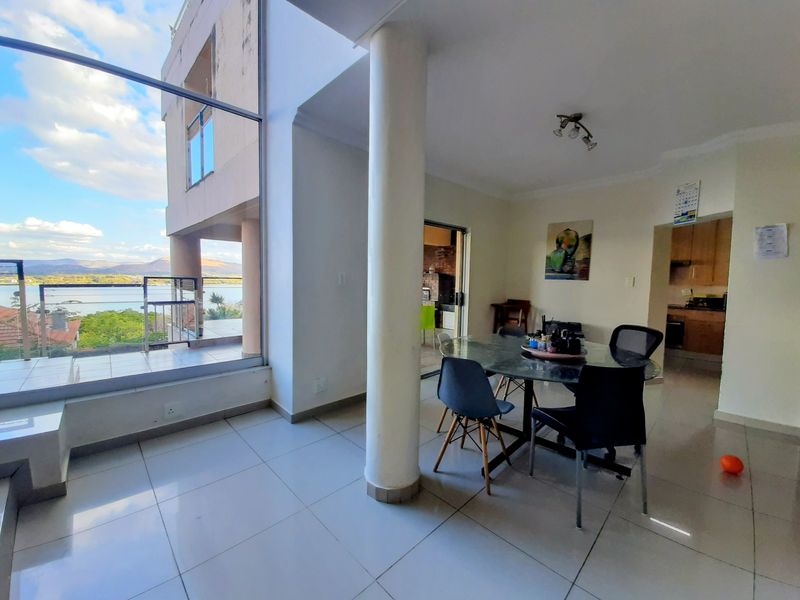 Open plan living and dining area featuring large floor-to-ceiling windows with scenic views, tiled flooring, and direct access to an outdoor balcony.