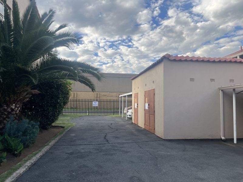 Exterior view of a paved driveway area featuring a carport, perimeter steel fencing, and a structure with a tiled roof.