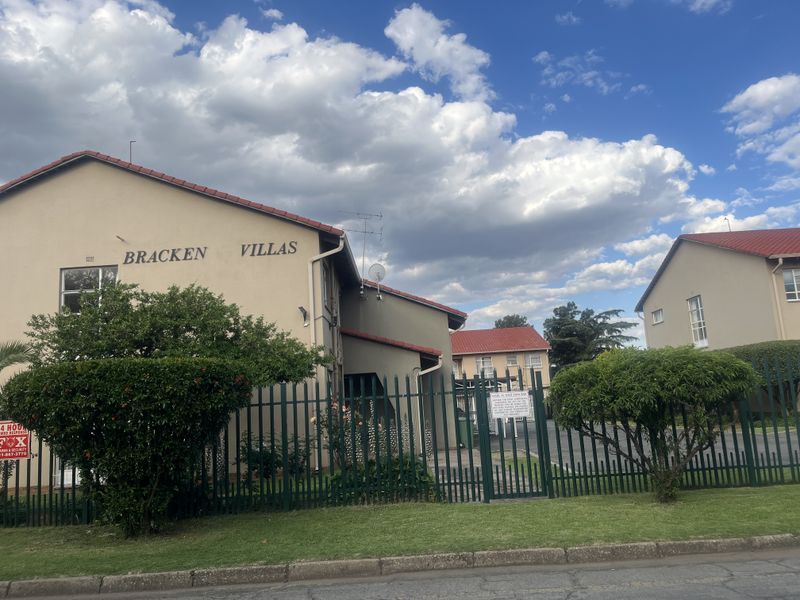 Exterior view of Bracken Villas apartment complex featuring a secure gated entrance, paved driveway, and well-maintained building facades with tiled roofing.
