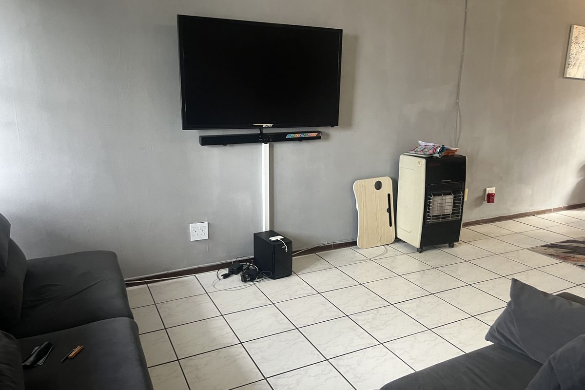 A living room featuring tiled flooring and a wall-mounted television with visible cable management trunking.