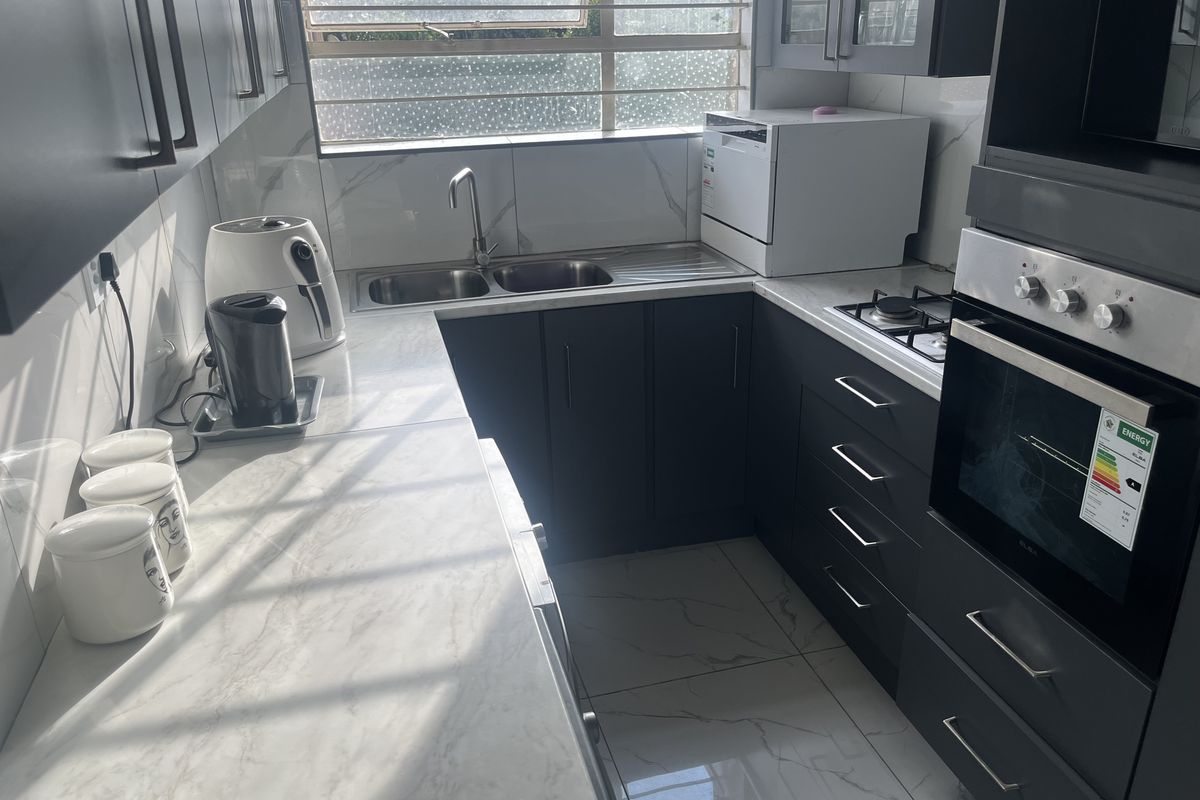 A modern kitchen featuring dark cabinetry, marble-look countertops, a double sink, and built-in oven with gas hob.