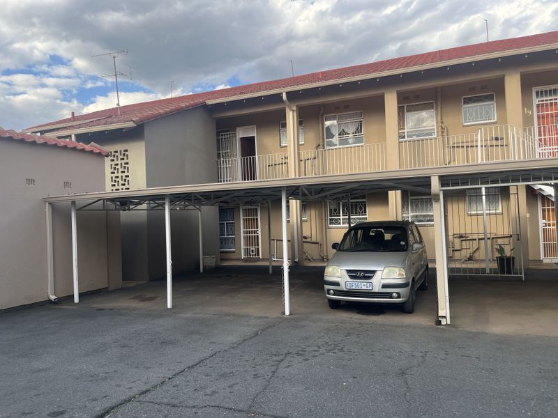 Exterior view of an apartment complex featuring a covered carport, paved driveway, and security-fitted windows and doors.