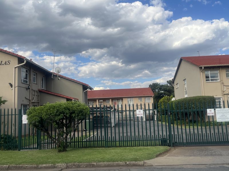 Front view of the apartment complex featuring a secure gated entrance, paved driveway, carports, and well-maintained exterior building facades with tiled roofs.