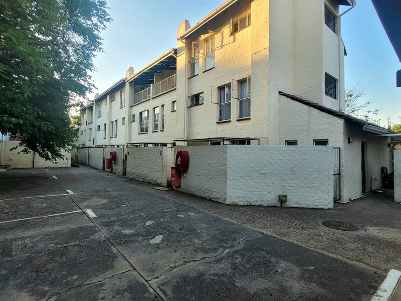 Exterior view of a multi-story townhouse complex featuring a paved driveway, painted brick boundary walls, and functional fire safety equipment.