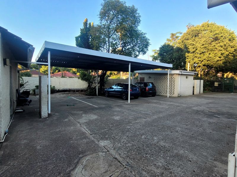 Outdoor parking area featuring a covered carport structure and concrete driveway with surrounding masonry boundary walls.