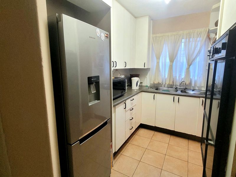 A functional kitchen featuring white built-in cabinetry, laminate countertops, a stainless steel sink, and tiled flooring, offering a practical layout for daily use.
