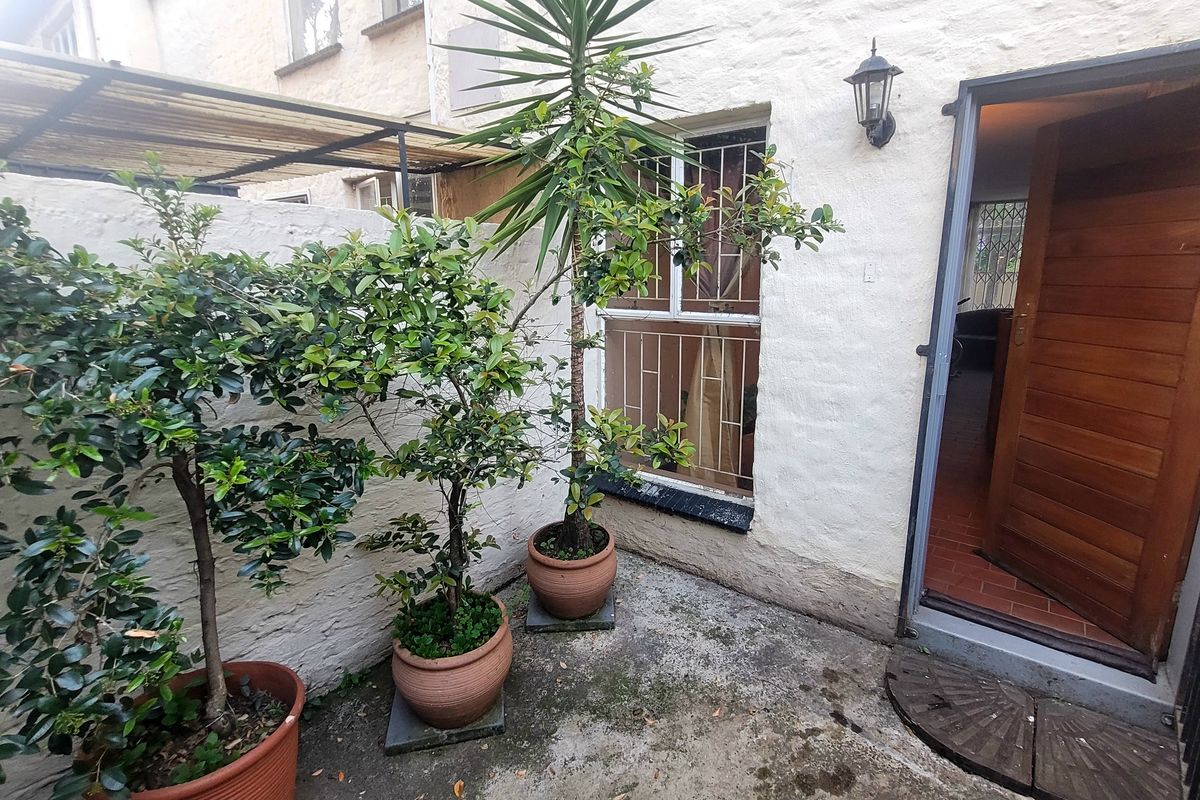 Rear exterior courtyard featuring a concrete patio, security-fitted window, and timber entrance door leading into the townhouse interior.