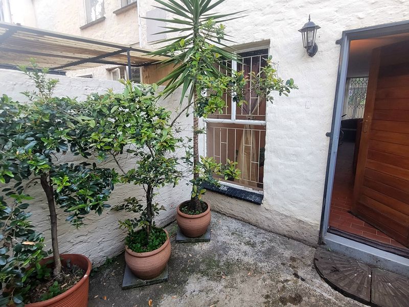 Rear exterior courtyard featuring a concrete patio, security-fitted window, and timber entrance door leading into the townhouse interior.