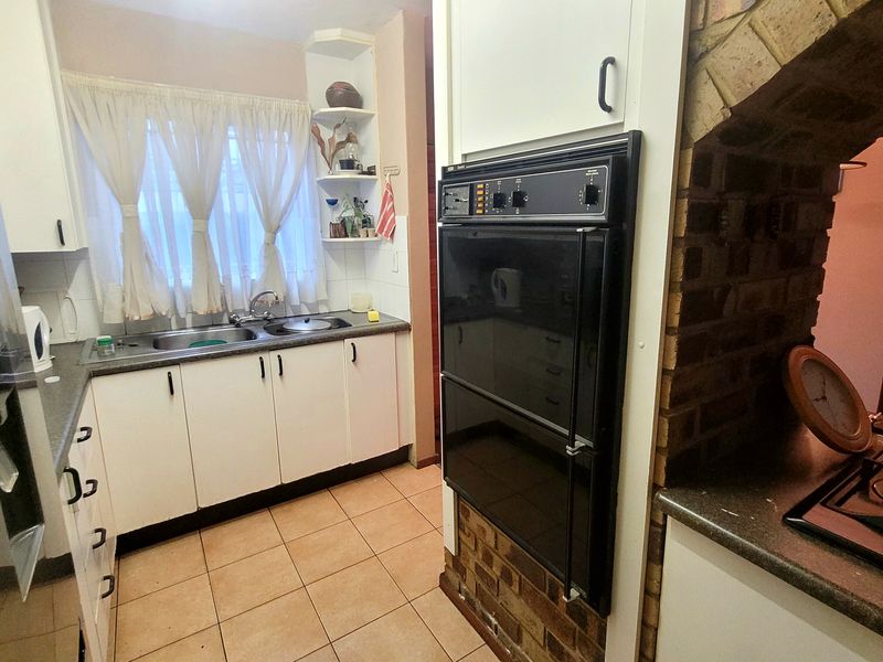 A functional kitchen featuring built-in double ovens, a hob, double sink, and classic cabinetry with a distinctive brick feature wall.
