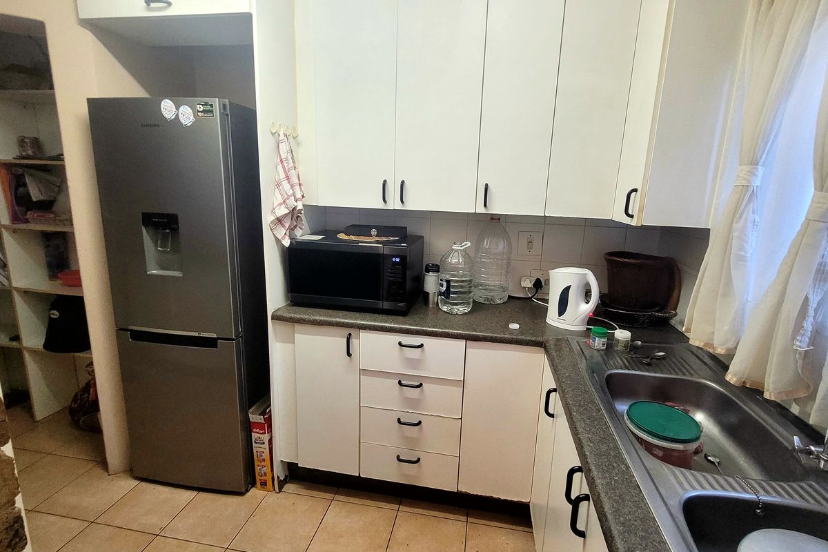 A functional kitchen featuring white cabinetry, laminate countertops, a stainless steel double sink, and tiled flooring, offering a practical layout for daily use.