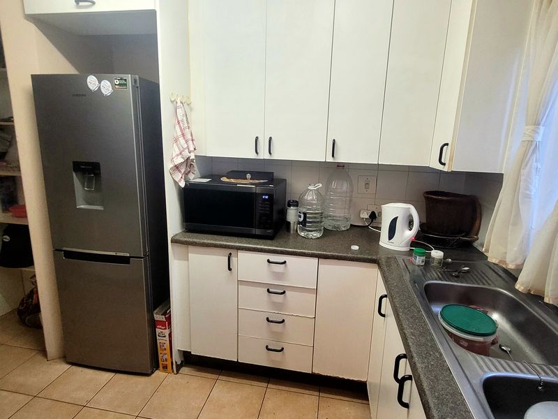 A functional kitchen featuring white cabinetry, laminate countertops, a stainless steel double sink, and tiled flooring, offering a practical layout for daily use.