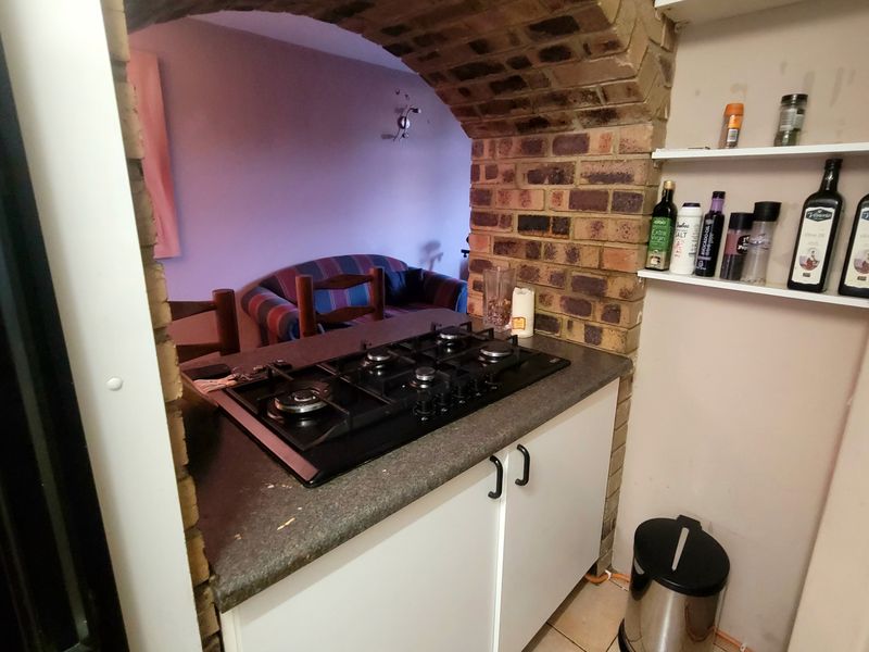 Compact kitchen area featuring a built-in gas hob, laminate countertops, and a distinctive exposed brick archway leading to the living space.