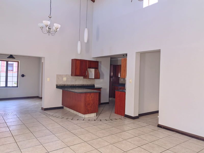 Spacious open-plan living area featuring high ceilings, tiled floors, and a functional kitchen with wooden cabinetry and granite countertops.
