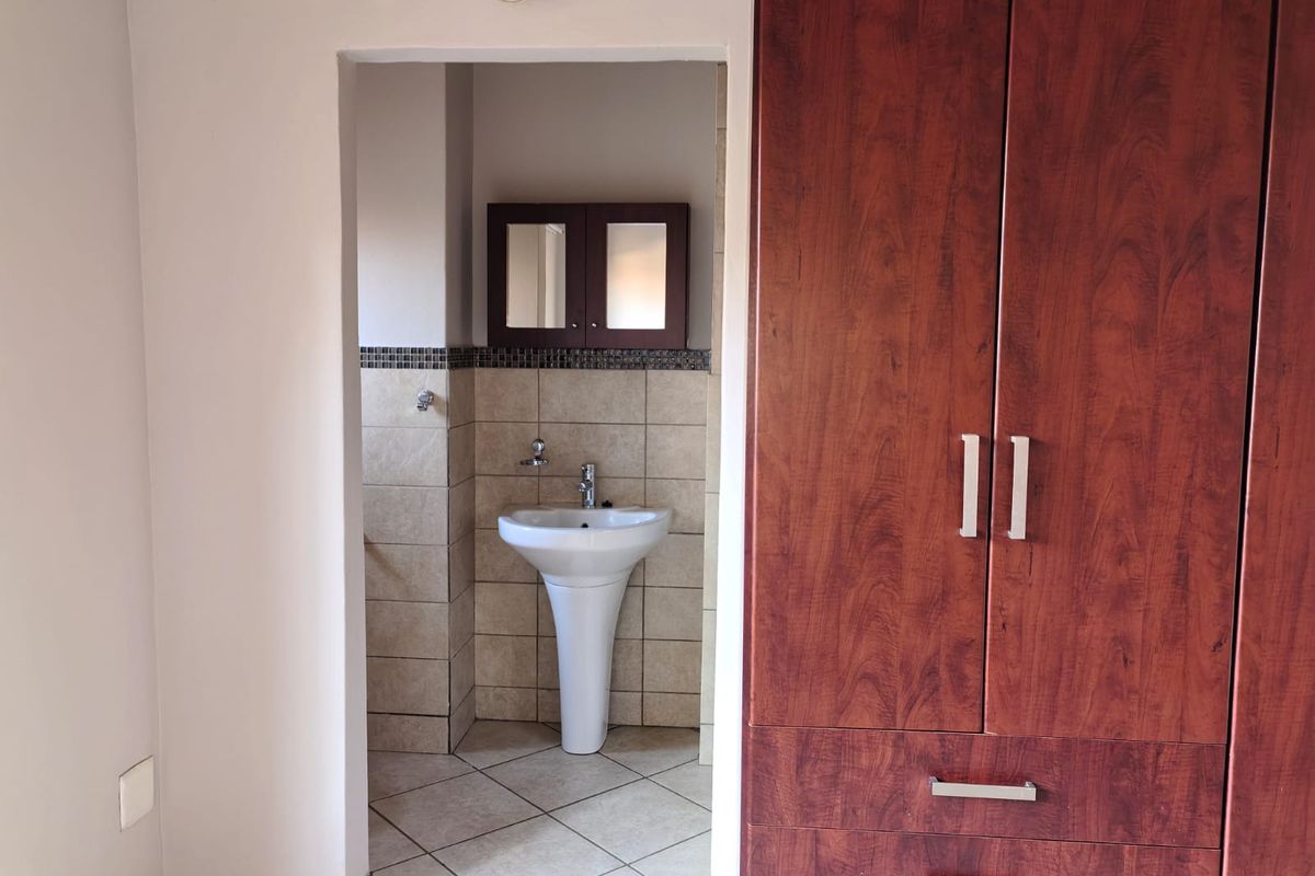 A functional bathroom featuring a pedestal basin, tiled splashback, and a built-in wooden cupboard for storage.