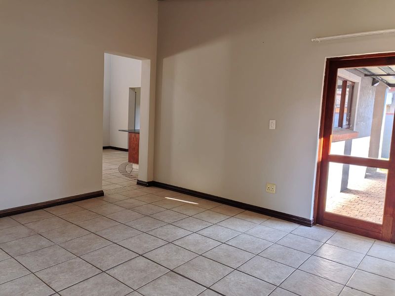 An empty living room featuring neutral tiled flooring, dark wood skirting, and a glass-paneled door leading to an outdoor area.