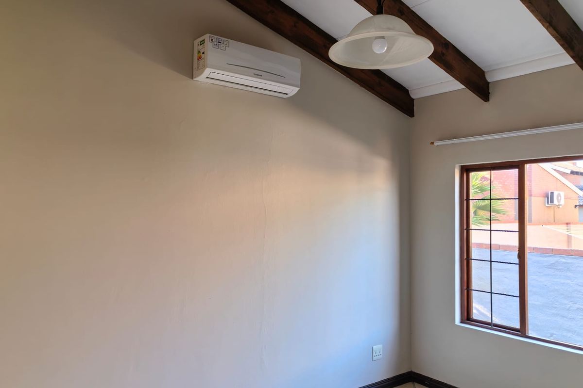 A bright, empty bedroom featuring exposed timber ceiling beams, tiled flooring, and a wall-mounted split-system air conditioner.