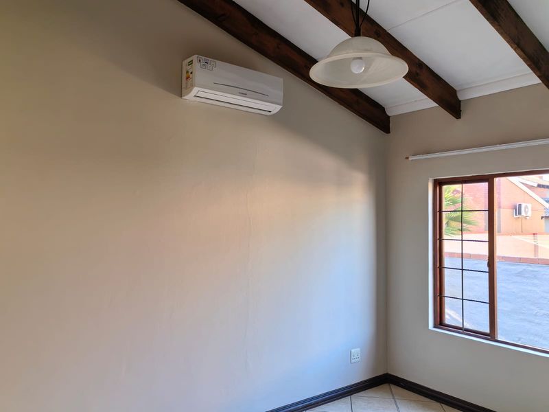 A bright, empty bedroom featuring exposed timber ceiling beams, tiled flooring, and a wall-mounted split-system air conditioner.