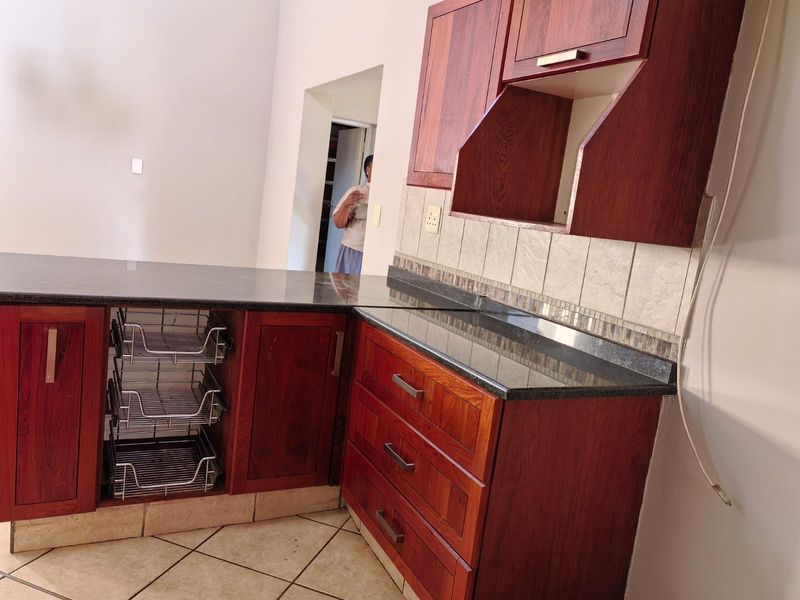 A kitchen area featuring dark wood cabinetry, granite countertops, a tiled backsplash, and pull-out wire storage drawers.