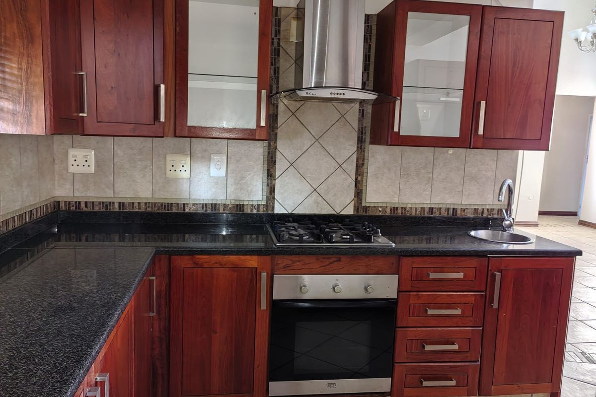 A well-maintained kitchen featuring dark wood cabinetry, granite countertops, a built-in gas hob, oven, and a stainless steel extractor fan.