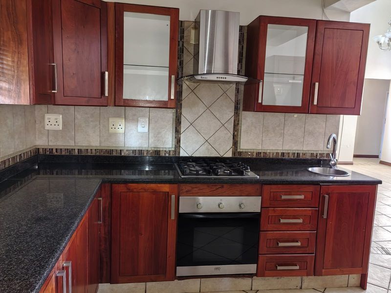 A well-maintained kitchen featuring dark wood cabinetry, granite countertops, a built-in gas hob, oven, and a stainless steel extractor fan.