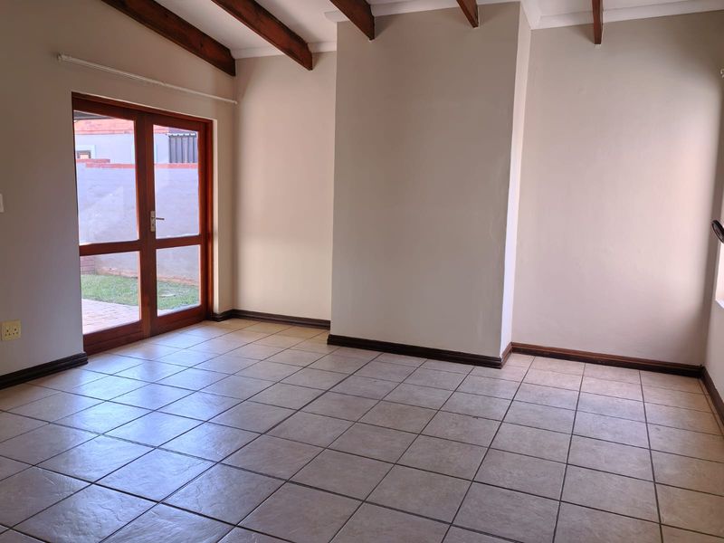 A bright, empty living room featuring tiled flooring, exposed timber ceiling beams, and timber-framed glass double doors leading to the exterior.