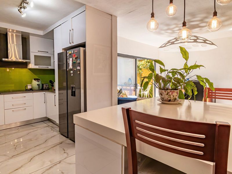 Modern open-plan kitchen and dining area featuring sleek white cabinetry, a vibrant green splashback, marble-look floor tiles, and direct access to an outdoor patio.