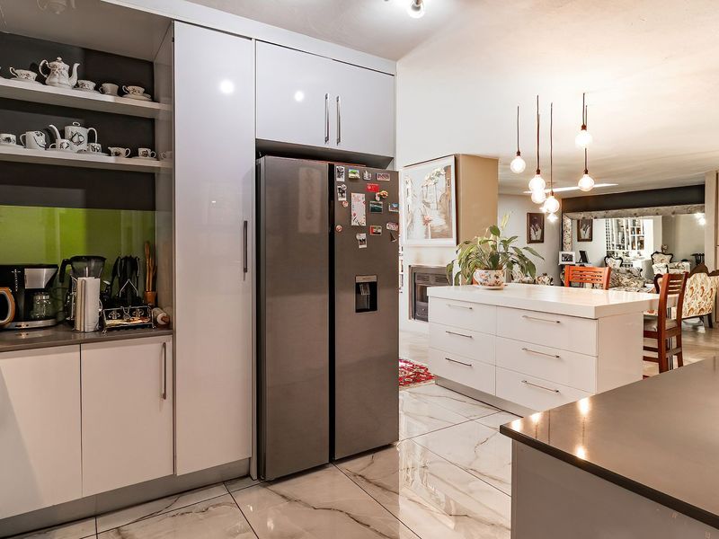 Modern open-plan kitchen featuring high-gloss cabinetry, stone countertops, and marble-look floor tiles, seamlessly flowing into the adjacent living and dining area.