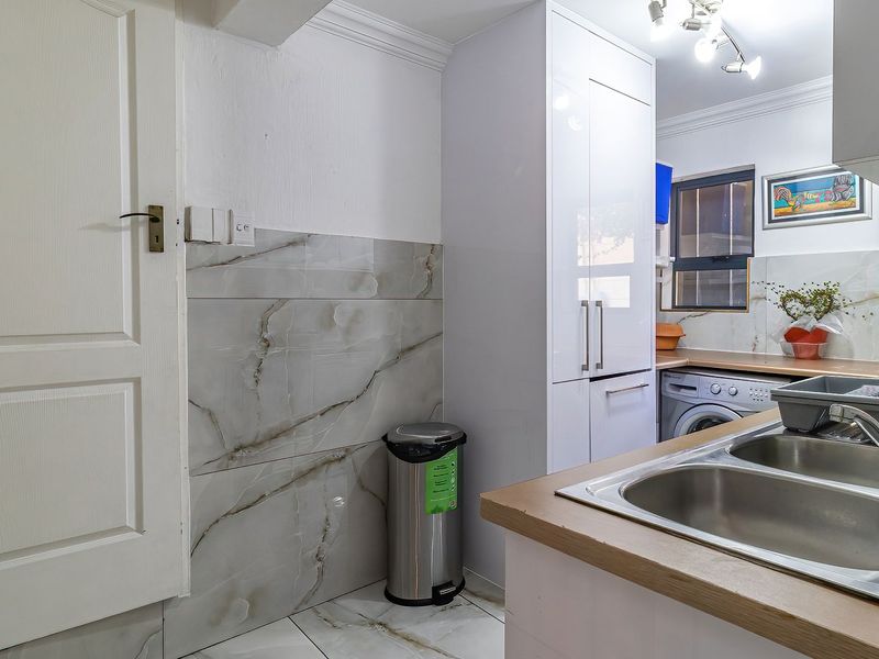 A functional laundry area featuring modern marble-look tiling, built-in cabinetry, and a double stainless steel sink with a mixer tap.