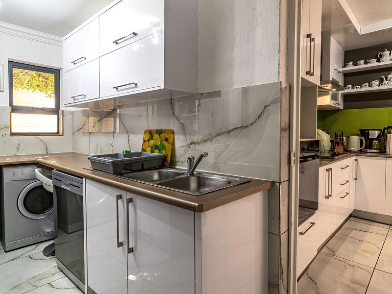 A modern, well-maintained scullery featuring sleek white cabinetry, marble-look wall tiles, and integrated appliances, providing a functional and organized secondary kitchen space.