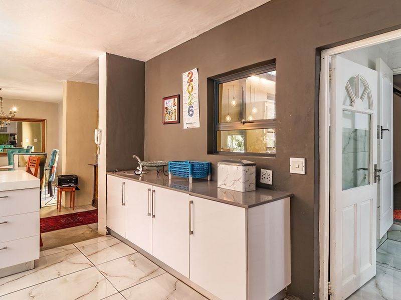 A functional scullery area featuring modern white cabinetry, stone countertops, a sink, and tiled flooring, providing convenient additional prep space.