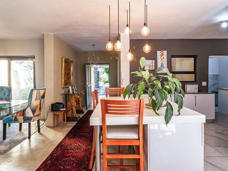 Spacious open-plan living and dining area featuring a central kitchen island, modern pendant lighting, and seamless access to the outdoor patio through sliding doors.