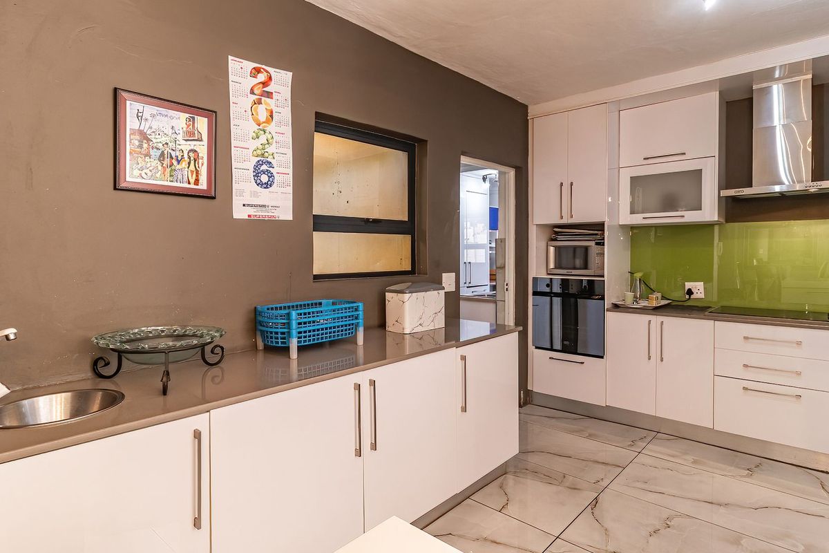 Modern kitchen featuring white cabinetry, stone countertops, integrated oven, extractor fan, and sleek tiled flooring with a glass splashback.