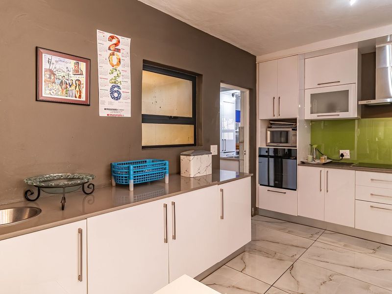 Modern kitchen featuring white cabinetry, stone countertops, integrated oven, extractor fan, and sleek tiled flooring with a glass splashback.