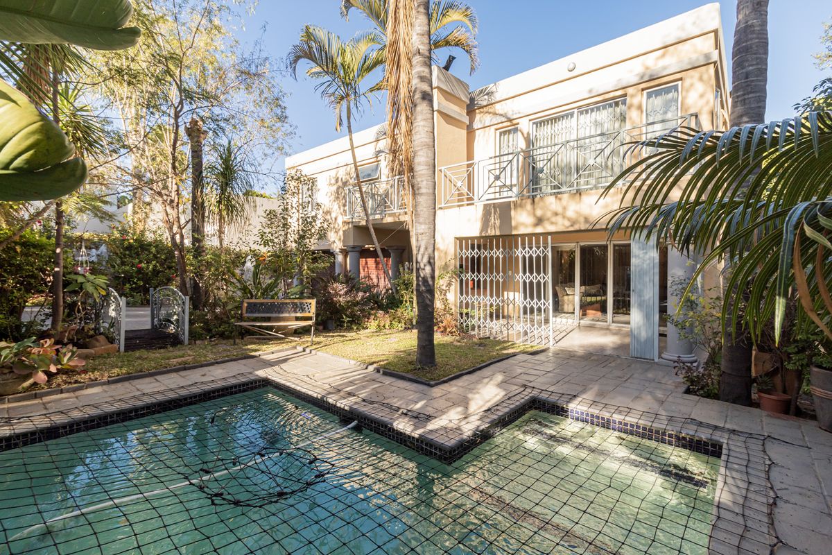 Rear view of the duet property featuring a swimming pool, paved patio area, and a balcony overlooking the private garden.