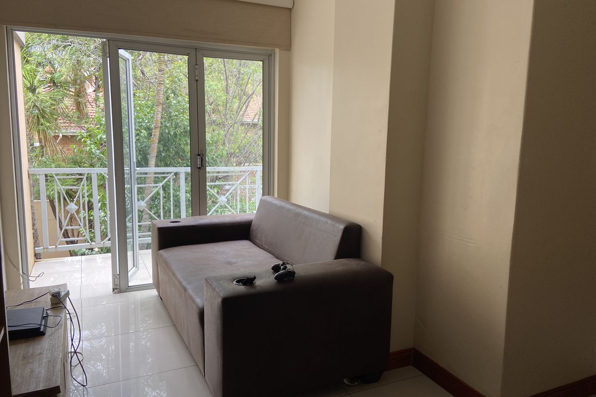 A living area featuring tiled flooring and large glass sliding doors that provide access to an outdoor balcony with garden views.