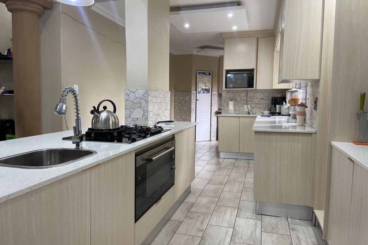 Modern kitchen featuring light wood cabinetry, stone countertops, a central island with a gas hob, and integrated appliances with neutral tiled flooring.