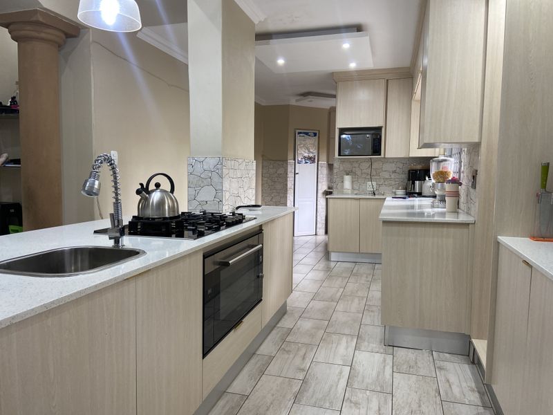 Modern kitchen featuring light wood cabinetry, stone countertops, a central island with a gas hob, and integrated appliances with neutral tiled flooring.