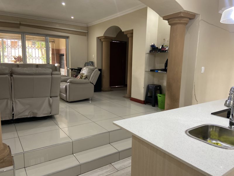 Open plan living area featuring tiled floors, decorative columns, and a kitchen island with an undermount sink, leading to a patio through sliding doors.