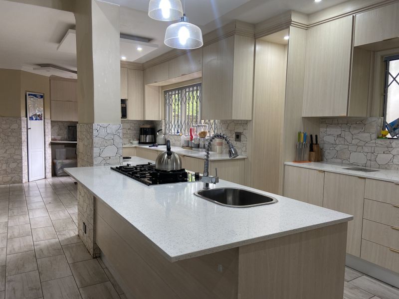 Modern kitchen featuring a central island with a gas hob, quartz countertops, ample built-in cabinetry, and stone tile backsplash accents.
