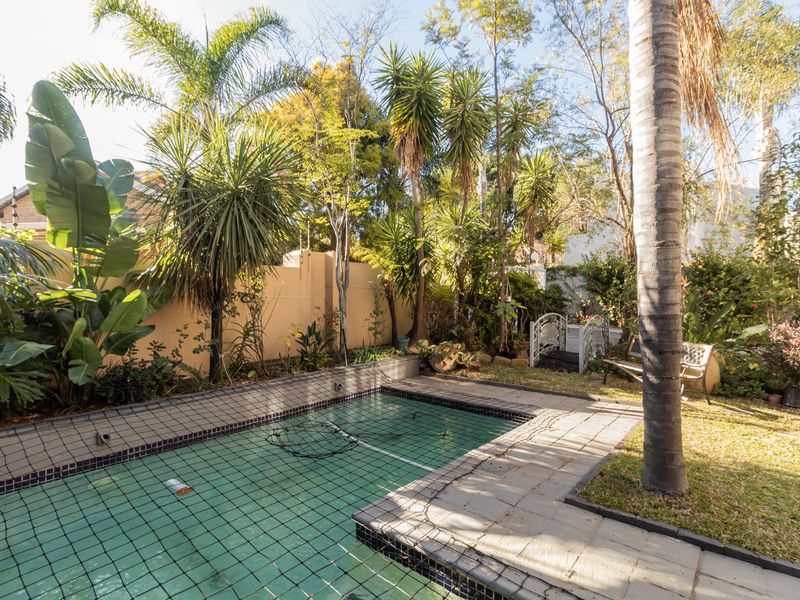 A private backyard pool area featuring a safety net, tiled surround, and established garden landscaping with mature trees and boundary walls.