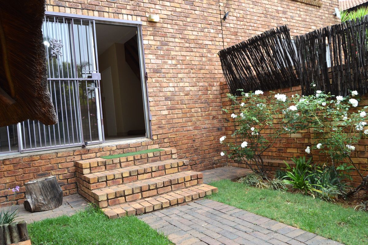 A rear exterior view of the townhouse featuring a brick facade, paved walkway, brick steps leading to a sliding glass door, and a timber screen fence.