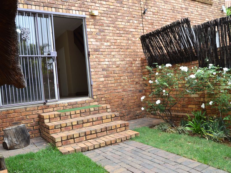 A rear exterior view of the townhouse featuring a brick facade, paved walkway, brick steps leading to a sliding glass door, and a timber screen fence.