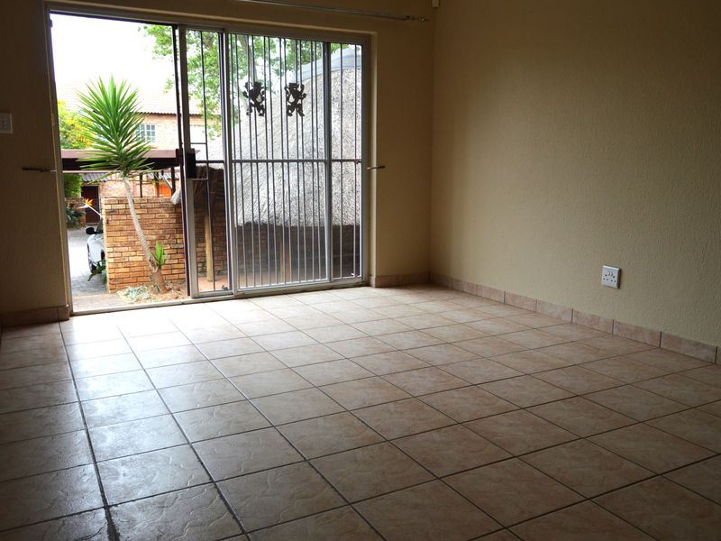 An empty living room featuring tiled flooring and a sliding glass door with a security gate, providing direct access to the outdoor area.