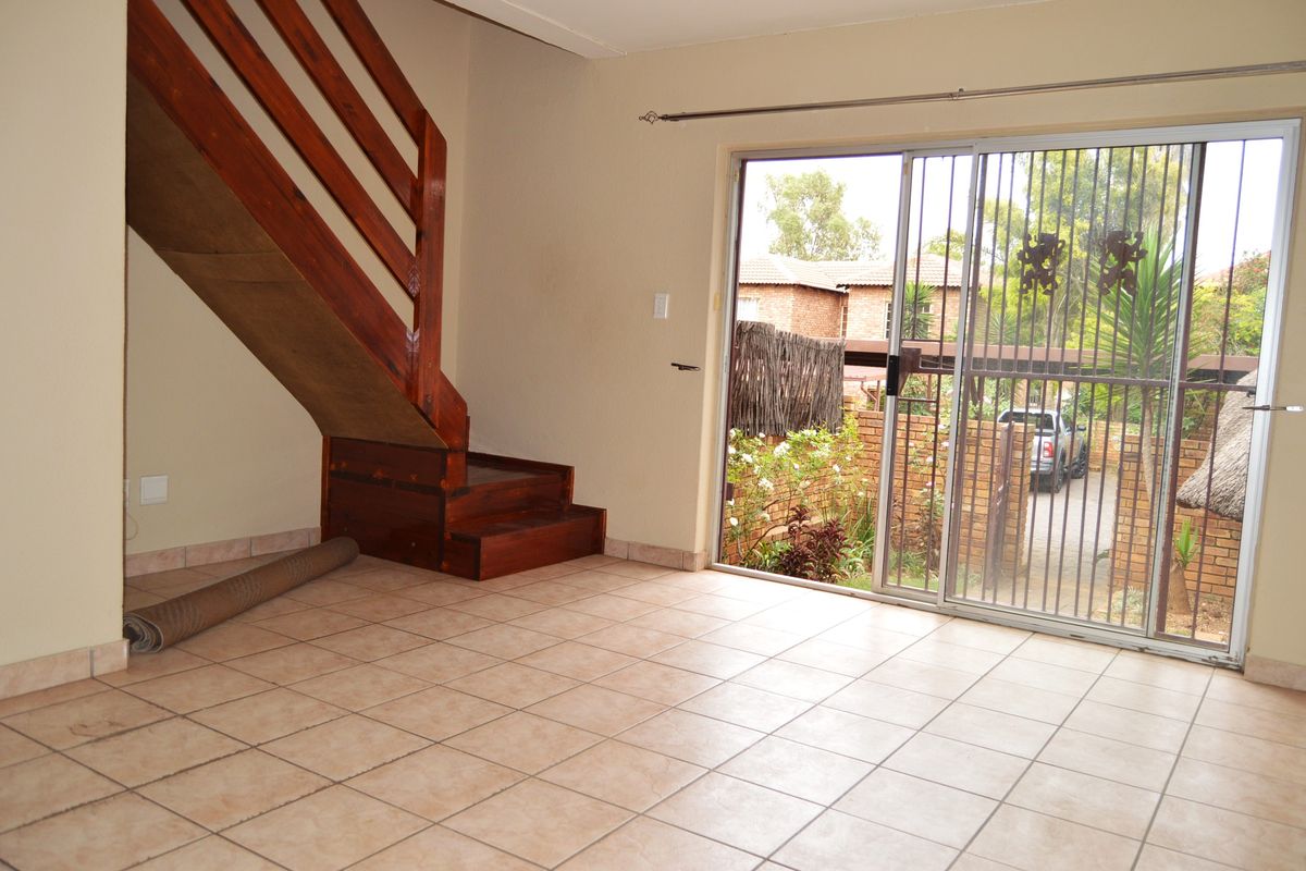 An empty living area featuring tiled flooring, a wooden staircase, and a sliding glass door with a security gate leading to the exterior.