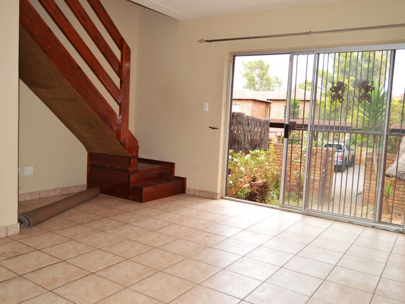 An empty living area featuring tiled flooring, a wooden staircase, and a sliding glass door with a security gate leading to the exterior.