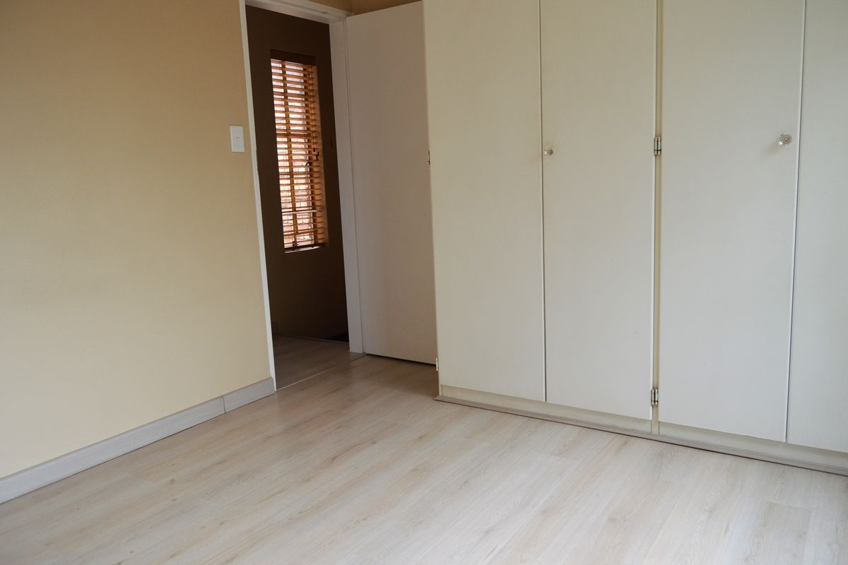 A clean, empty bedroom featuring light-toned laminate flooring and built-in cupboards, offering a neutral canvas for personalization.