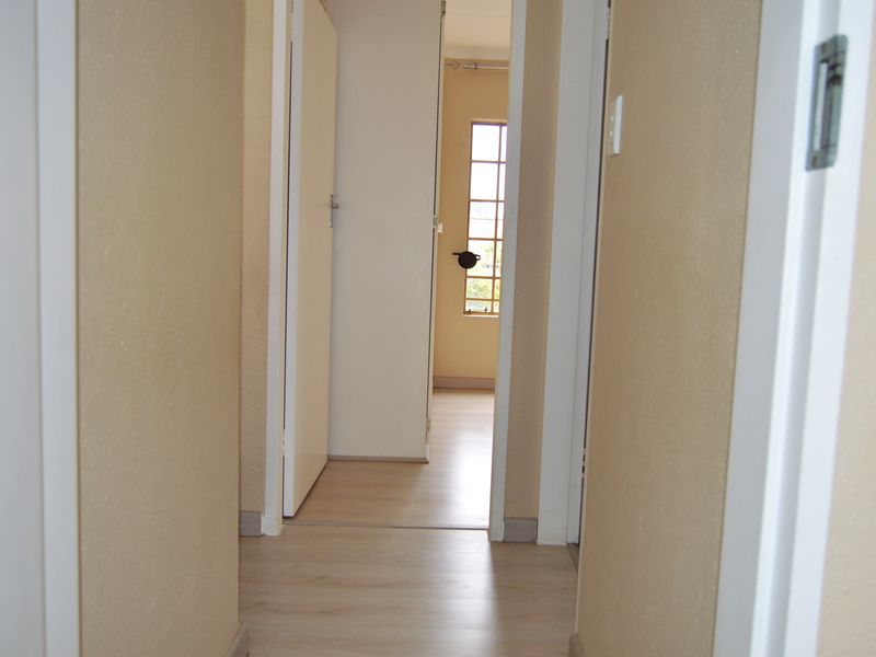 A clean, empty hallway featuring light-toned laminate flooring and neutral walls, providing access to adjacent rooms within the townhouse.